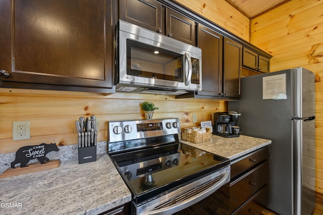 kitchen with light stone countertops, dark brown cabinets, stainless steel appliances, and wood walls