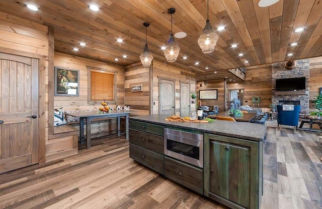 kitchen with built in microwave, a fireplace, pendant lighting, and wood walls