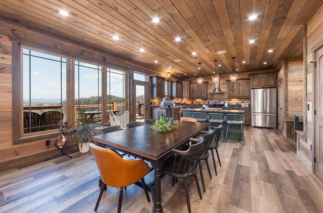 dining space with light wood-type flooring, wooden ceiling, and wood walls