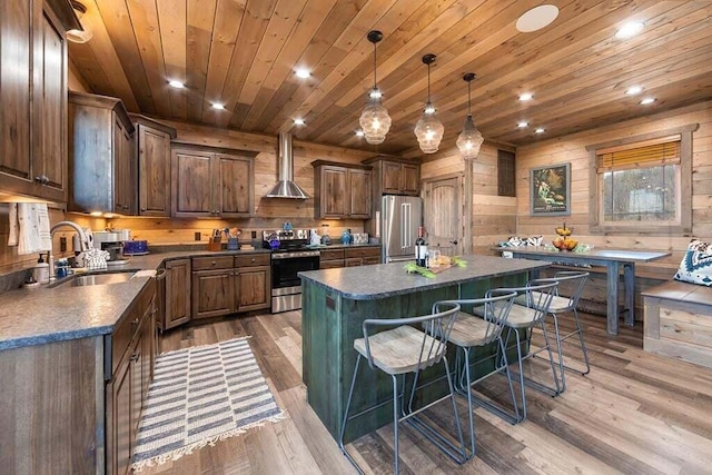 kitchen featuring wall chimney exhaust hood, stainless steel appliances, sink, pendant lighting, and a kitchen island