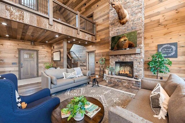 living room featuring a high ceiling, wooden ceiling, a stone fireplace, and wooden walls