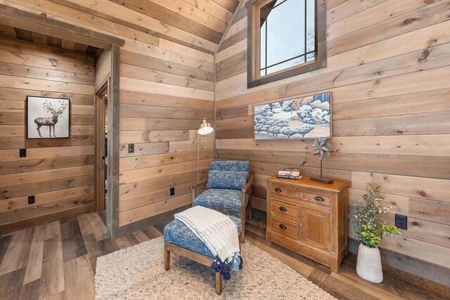 sitting room with wood walls, dark wood-type flooring, and vaulted ceiling