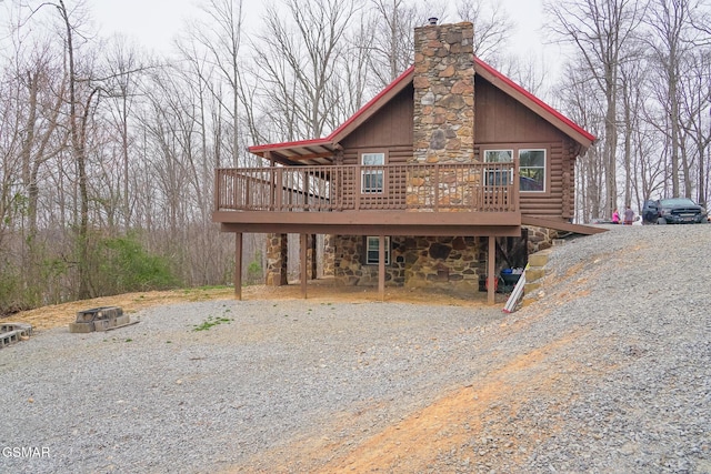 cabin with gravel driveway, log exterior, stone siding, and a chimney