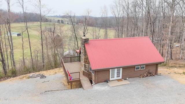 view of front of home featuring a forest view, log siding, french doors, a chimney, and metal roof