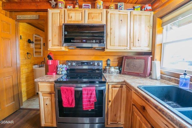 kitchen with a sink, dark wood finished floors, appliances with stainless steel finishes, wood walls, and light countertops