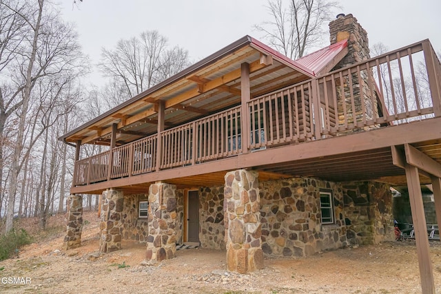 rear view of property featuring a deck, a chimney, stone siding, and metal roof