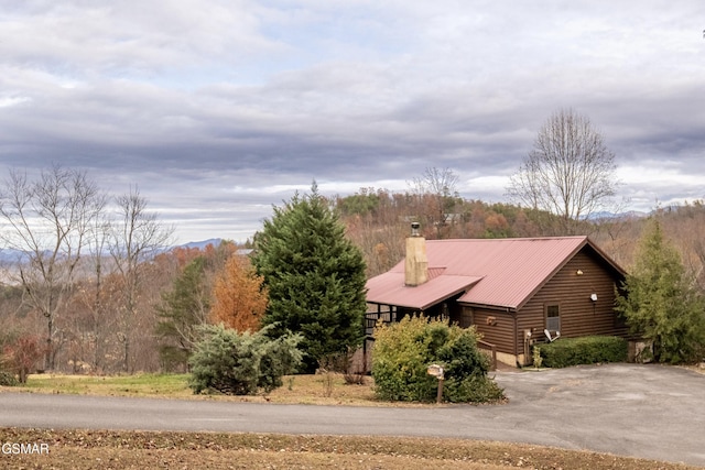 view of home's exterior with metal roof, a chimney, log siding, and a wooded view