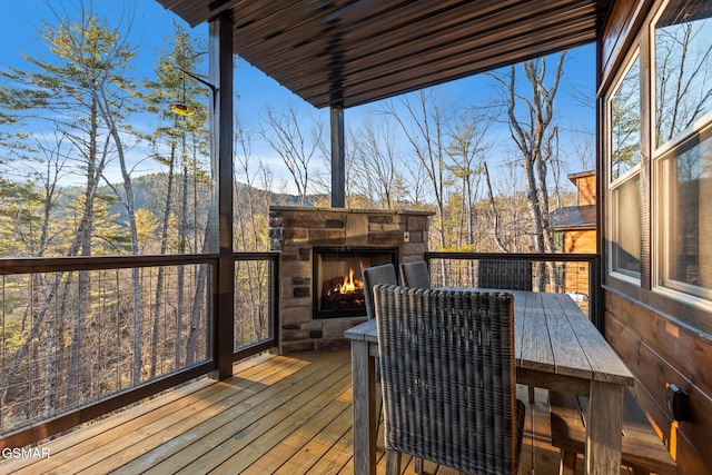 deck with a lit fireplace and outdoor dining area