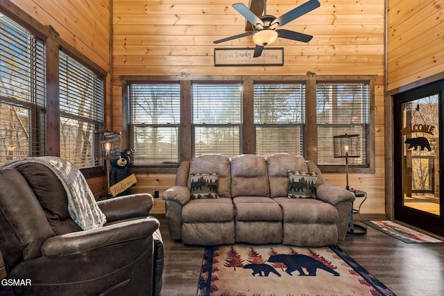 living area with ceiling fan, wood walls, wood finished floors, and a towering ceiling