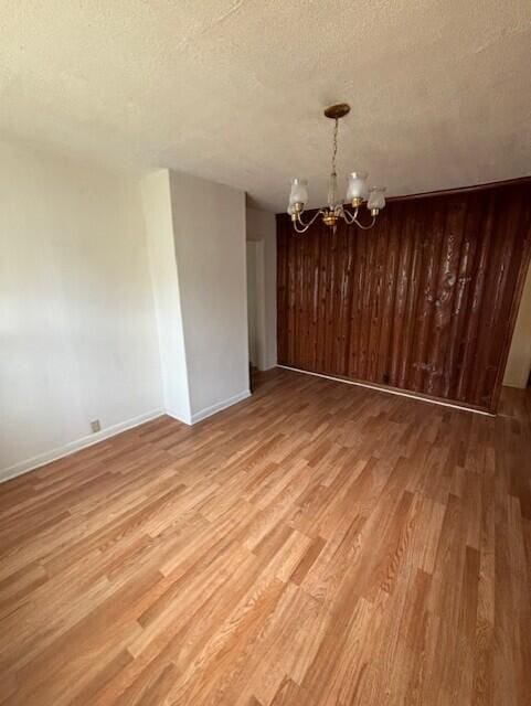 unfurnished dining area with light hardwood / wood-style floors, a textured ceiling, and a chandelier