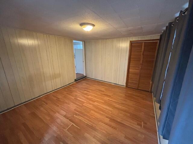 unfurnished bedroom featuring light hardwood / wood-style flooring, wooden walls, and a closet