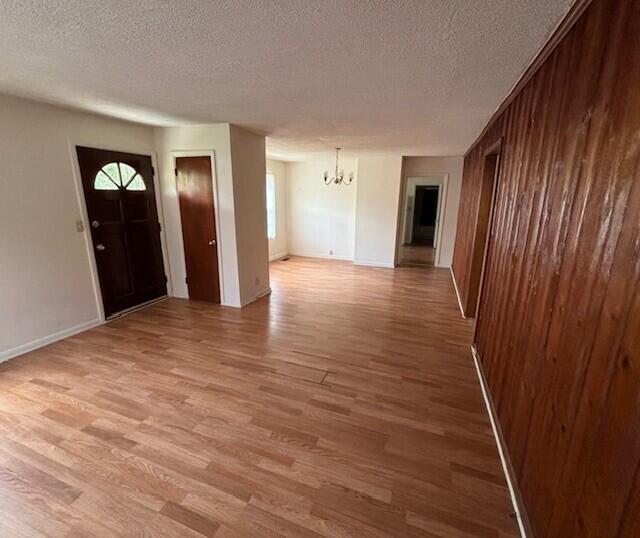 interior space with wooden walls, light hardwood / wood-style floors, a textured ceiling, and a notable chandelier