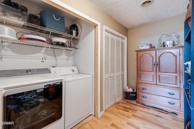 laundry room featuring washing machine and clothes dryer, light hardwood / wood-style flooring, and a textured ceiling