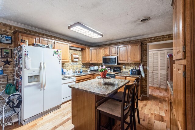 kitchen featuring light wood-type flooring, white appliances, a kitchen island, and brick wall