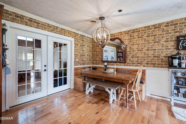 dining area with french doors, brick wall, a textured ceiling, and light hardwood / wood-style floors