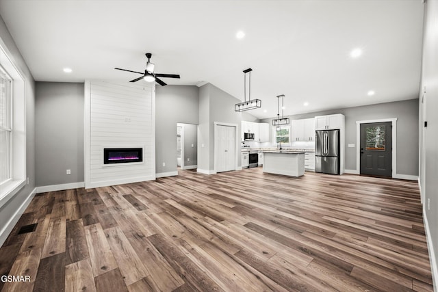 unfurnished living room featuring ceiling fan, lofted ceiling, a fireplace, and wood-type flooring