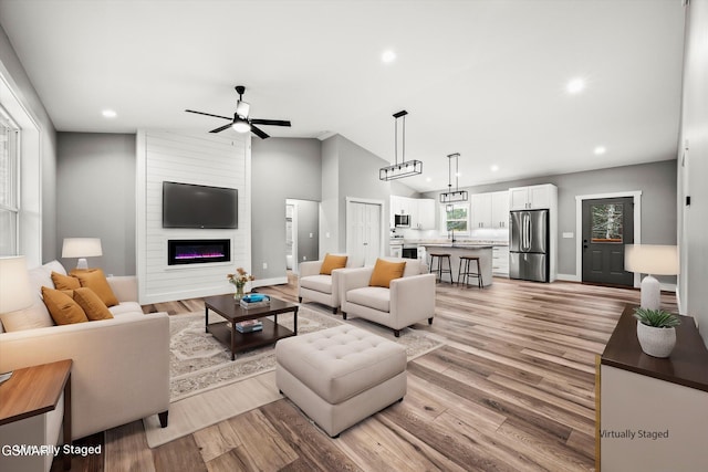 living room featuring ceiling fan, lofted ceiling, a fireplace, and light hardwood / wood-style flooring