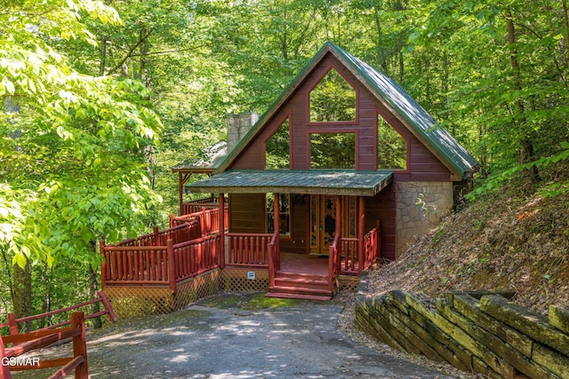 chalet / cabin featuring a wooded view, a chimney, and stone siding