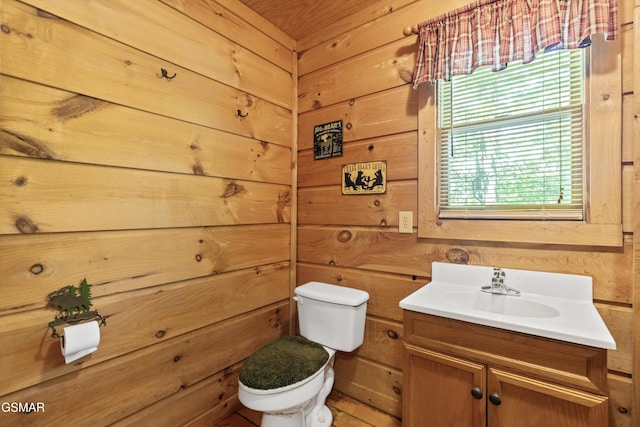 bathroom featuring toilet, vanity, healthy amount of natural light, and wood walls