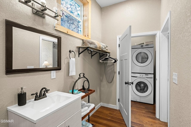 laundry area with laundry area, a textured wall, dark wood-style floors, stacked washer / drying machine, and a sink