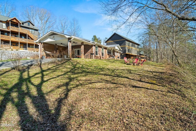 back of property featuring brick siding, an attached carport, ceiling fan, a yard, and driveway