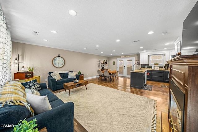 living area featuring visible vents, a textured ceiling, wood finished floors, and crown molding