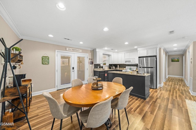 dining room with visible vents, light wood-style floors, and ornamental molding