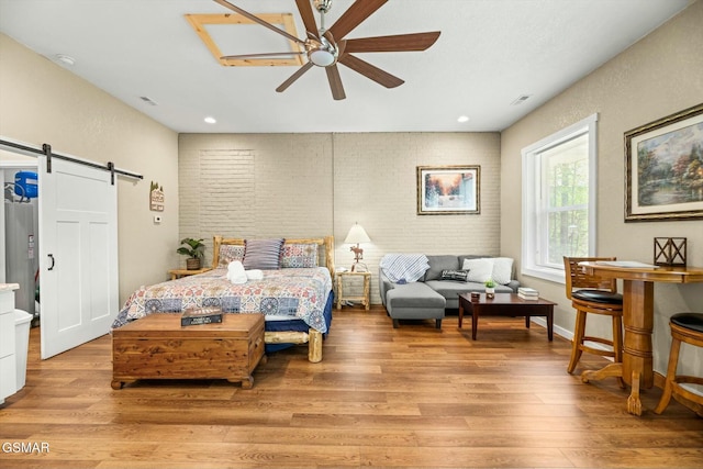 bedroom featuring a barn door, ceiling fan, brick wall, and light wood-style floors