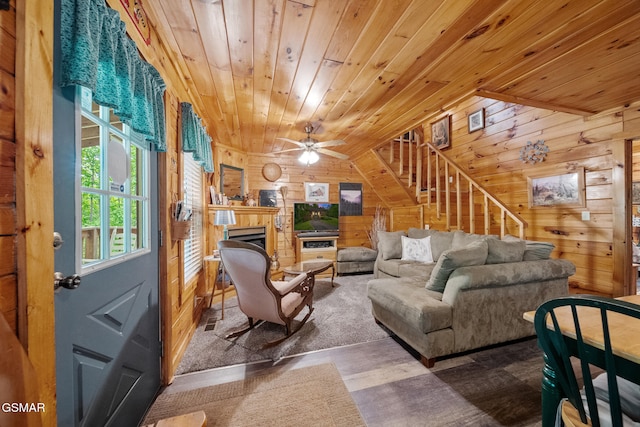 living area with wooden ceiling, wood walls, stairs, a fireplace, and ceiling fan
