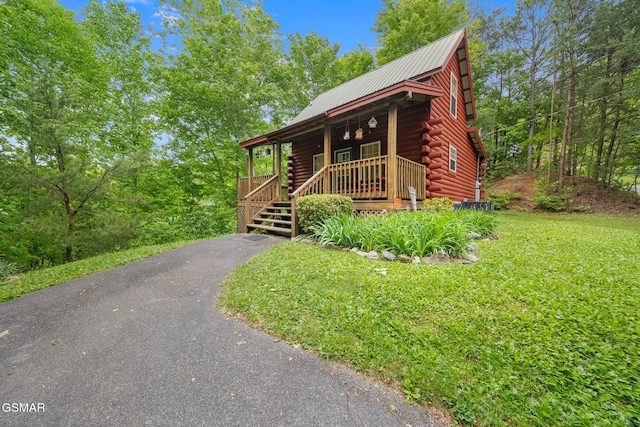 log cabin with log siding, covered porch, metal roof, a front lawn, and driveway