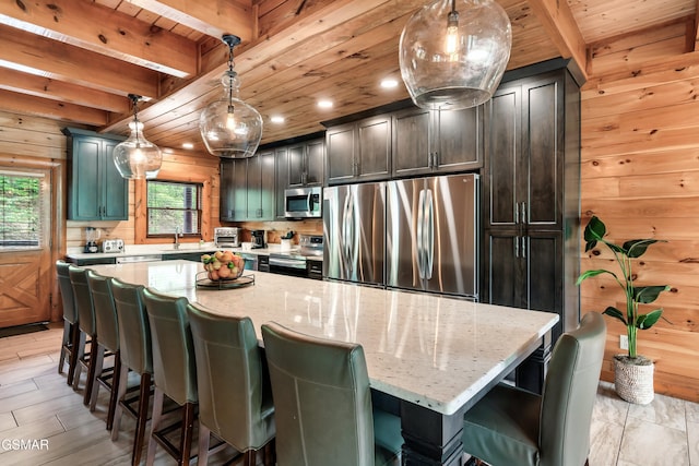 kitchen featuring pendant lighting, light stone countertops, beamed ceiling, a kitchen island, and stainless steel appliances