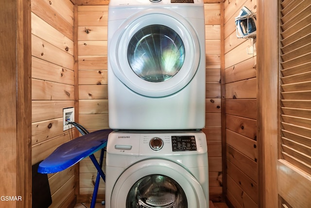 laundry area featuring stacked washer / drying machine and wooden walls