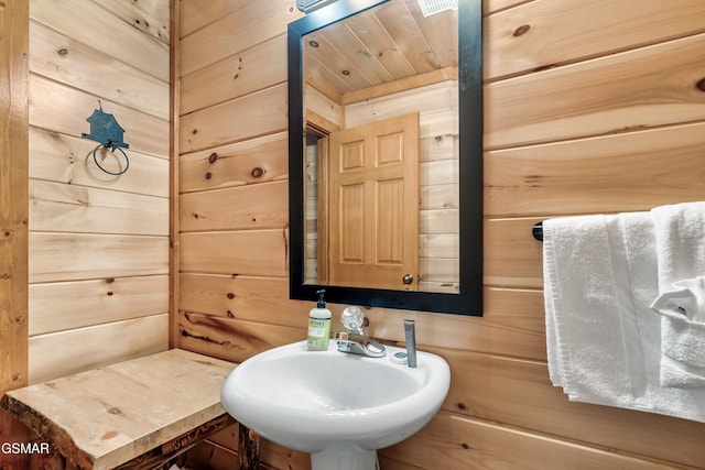 bathroom with wood ceiling, sink, and wooden walls