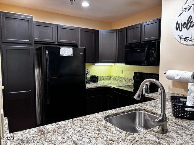 kitchen with light stone countertops, black appliances, dark cabinetry, and a sink