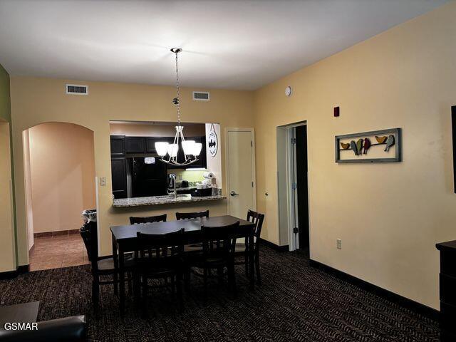 dining area with arched walkways, visible vents, dark colored carpet, and an inviting chandelier