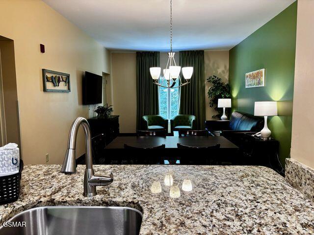 kitchen with light stone counters, open floor plan, hanging light fixtures, a sink, and a notable chandelier