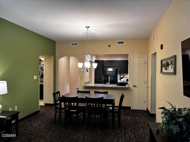 dining space featuring arched walkways, visible vents, and dark carpet