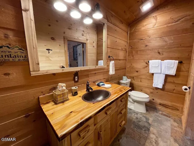 bathroom with wooden walls, vanity, toilet, stone finish flooring, and vaulted ceiling