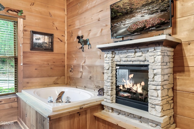 bathroom featuring wooden walls, plenty of natural light, a fireplace, and a garden tub