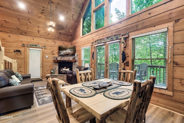 dining room with wooden walls, high vaulted ceiling, light wood-type flooring, and a healthy amount of sunlight