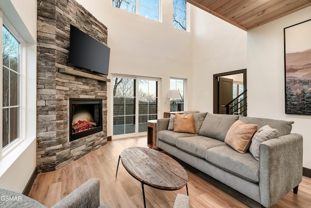 living room featuring wood ceiling, a fireplace, a high ceiling, and light wood-type flooring