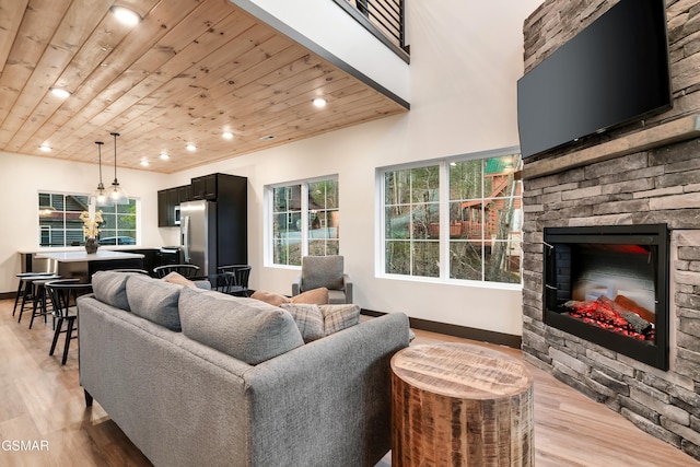 living room with wood ceiling, a stone fireplace, and light hardwood / wood-style flooring