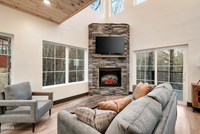 living room with a high ceiling, a stone fireplace, wooden ceiling, and light wood-type flooring