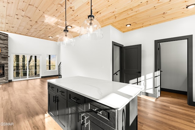 kitchen featuring wood ceiling, decorative light fixtures, a center island, a fireplace, and light stone countertops