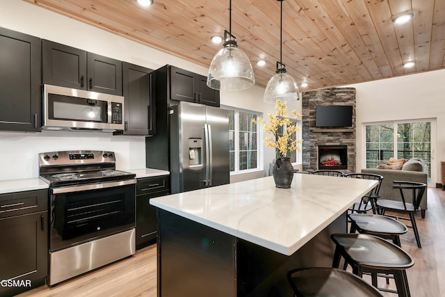 kitchen featuring appliances with stainless steel finishes, decorative light fixtures, a breakfast bar area, a center island, and wooden ceiling