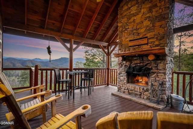 deck at dusk featuring a mountain view and an outdoor stone fireplace