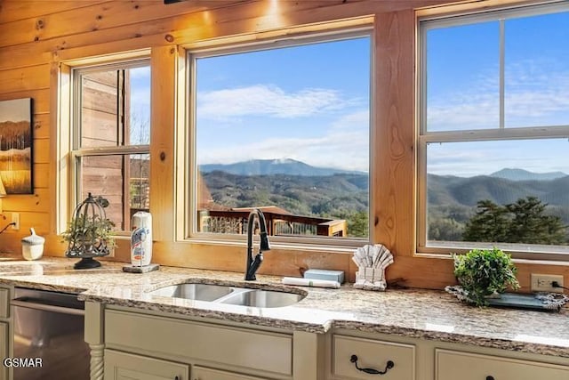 kitchen with light stone counters, stainless steel dishwasher, a mountain view, white cabinetry, and a sink