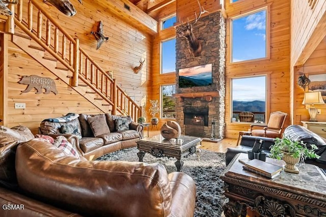 living room featuring wood walls, stairs, beam ceiling, a stone fireplace, and a high ceiling