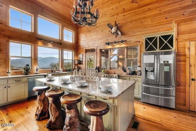 kitchen with wood walls, stainless steel appliances, light wood-style flooring, and a towering ceiling