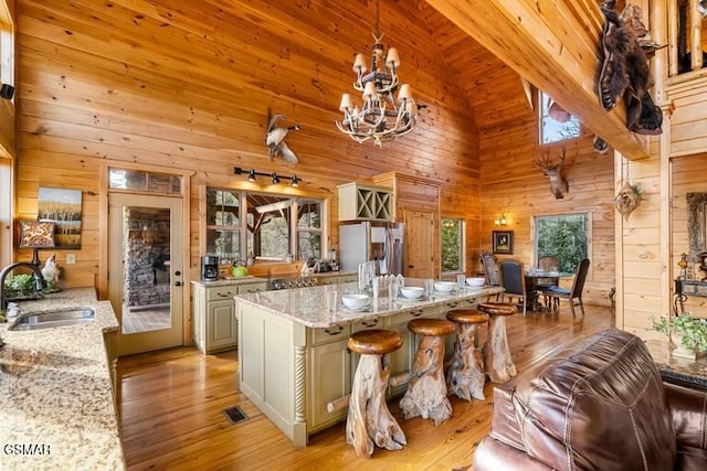 kitchen featuring light wood-type flooring, stainless steel refrigerator with ice dispenser, wood walls, and a sink